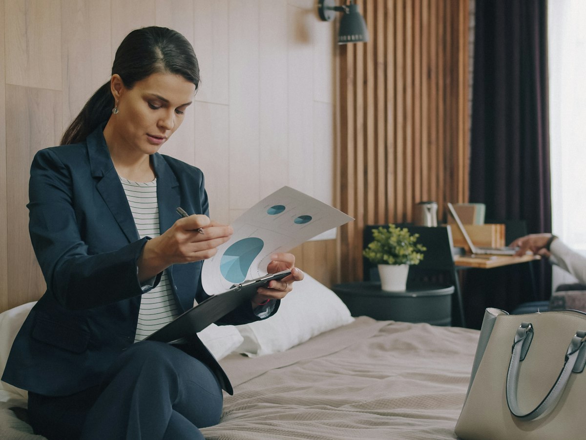 A woman in a suit reviewing charts on a bed in a hotel room - EventGear PDX